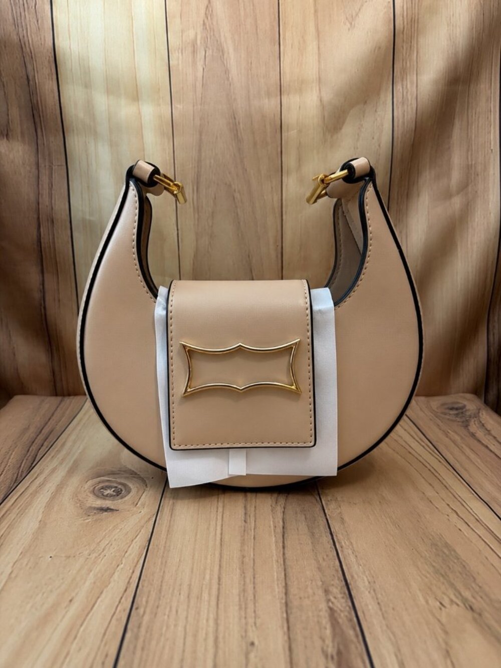 small Tan crescent-shaped handbag featuring sleek black trim, gold-tone hardware